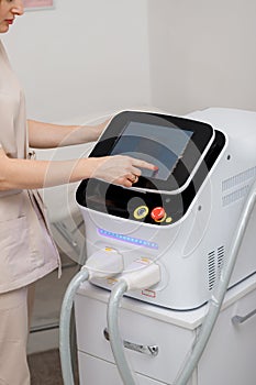 Beautician holding ultrasound device for face and skin lifting procedure and hair removal. Young woman cosmetologist using modern