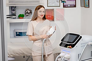 Beautician holding ultrasound device for face and skin lifting procedure and hair removal. Young woman cosmetologist using modern