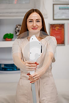 Beautician holding ultrasound device for face and skin lifting procedure and hair removal. Young woman cosmetologist using modern