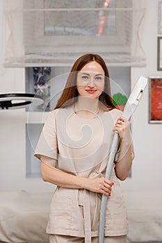 Beautician holding ultrasound device for face and skin lifting procedure and hair removal. Young woman cosmetologist using modern