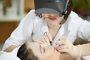 Beautician in magnifying lenses does epilation on photo