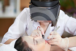 Beautician in magnifying lenses does epilation on photo