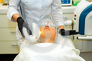 Beautician makes anti-aging procedure for women in the beauty salon. Doctor in medical gloves, patient in special glasses