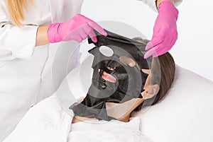 Beautician makes a black face mask of a woman to rejuvenate the skin. Cosmetology treatment of problem skin on the face and body