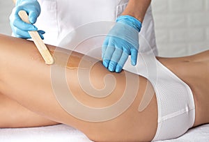 A beautician makes a depilation of a woman`s legs in a beauty salon. Female aesthetic cosmetology