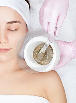 Beautician makes a face clay mask against acne on the face of a woman to rejuvenate the skin. Cosmetology treatment of problem