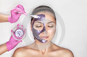 Beautician makes a face mask with purple particles on the face of a woman to rejuvenate the skin. Cosmetology treatment of problem