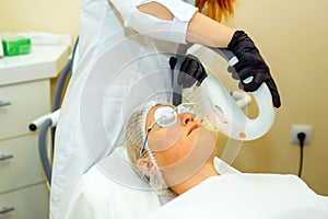 Beautician makes facial rejuvenation procedure for women in the beauty salon. Doctor in medical gloves, patient in special glasses