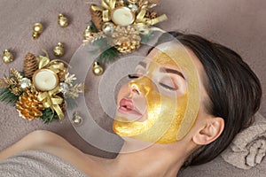 Beautician makes a golden mask to rejuvenate the skin to beautiful woman. Next to her are Christmas decorations.New Year`s and