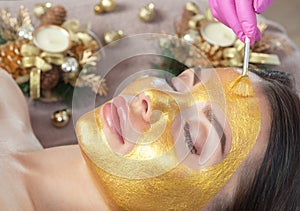 Beautician makes a golden mask to rejuvenate the skin to beautiful woman. Next to her are Christmas decorations.New Year`s and