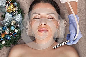 Beautician makes a procedure Microdermabrasion to beautiful woman. Next to her are Christmas decorations. New Year`s and