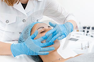 Beautician makes professional massage of the patient`s face. A young girl is undergoing a course of spa treatments in the office