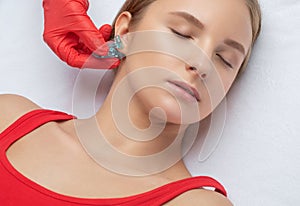 A beautician makes a puncture of the earlobe with a disposable device in a beauty salon. Ear piercing