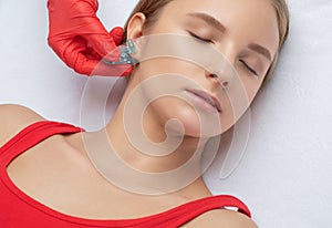 A beautician makes a puncture of the earlobe with a disposable device in a beauty salon. Ear piercing photo