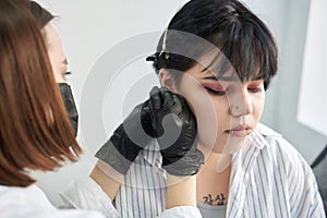 A beautician makes a puncture of the earlobe with a disposable device in a beauty salon. Ear piercing lobe.