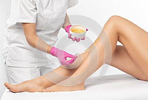 A beautician makes a sugar paste depilation of a woman`s legs in a beauty salon