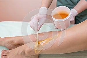A beautician makes a sugar paste depilation of a woman`s legs in a beauty salon