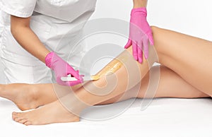 A beautician makes a sugar paste depilation of a woman`s legs in a beauty salon. Female aesthetic cosmetology