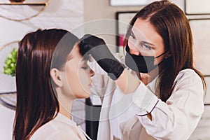 Beautician- makeup artist applies paint henna on previously plucked, design, trimmed eyebrows in a beauty salon in the