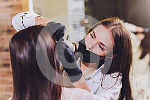 Beautician- makeup artist applies paint henna on previously plucked, design, trimmed eyebrows in a beauty salon in the