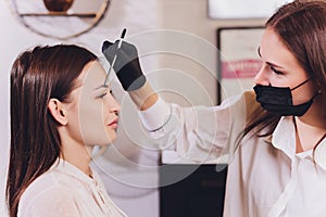 Beautician- makeup artist applies paint henna on previously plucked, design, trimmed eyebrows in a beauty salon in the