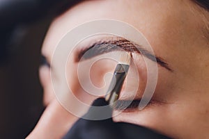 Beautician- makeup artist applies paint henna on previously plucked, design, trimmed eyebrows in a beauty salon in the