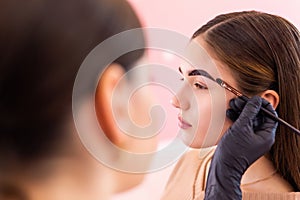 beautician- makeup artist applies paint henna on previously plucked, design, trimmed eyebrows in a beauty salon in the session