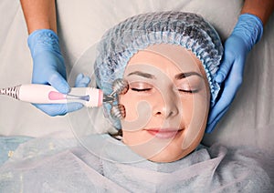 Beautician massaging woman face with facial roller.