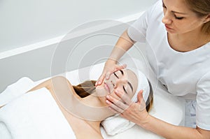 Beautician massaging woman`s face. Attractive girl having facial treatment and massage