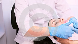 The beautician in medical gloves dabs the patient woman chin with a napkin to removes the remaining cream, cosmetology