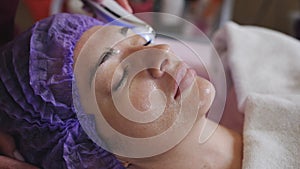 Beautician with microdermabrasion device doing face exfoliation to young woman lying at spa