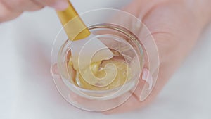 Beautician mixing face mask in glass bowl using brush, hands close-up.