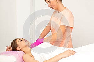 Beautician with a patient during sugaring. The cosmetologist waxes the female armpit.