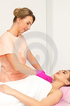 Beautician with a patient during sugaring. The cosmetologist waxes the female armpit.