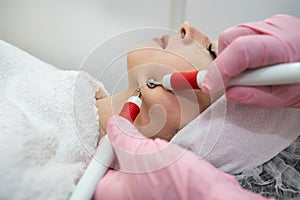 beautician performing microcurrent stimulation young woman on face at spa clinic