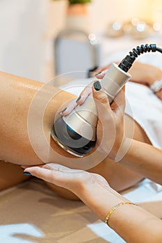 Beautician performing ultrasonic cavitation treatment on a woman& x27;s leg. Anti cellulite. Close up