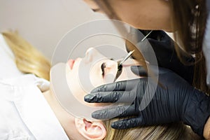 Beautician performs eyebrow correction on a beautiful model in a beauty salon. The girl is blonde. Facial treatment. Henna dyeing