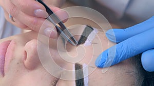 Beautician plucking eyebrows with tweezers to woman in beauty salon.