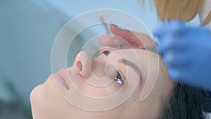 Beautician plucking eyebrows with tweezers to woman in beauty salon, closeup.