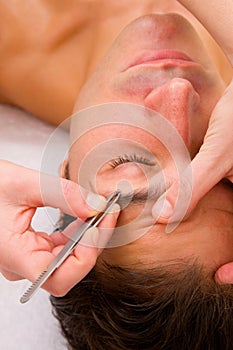 Beautician plucking a man eyebrows with tweezers