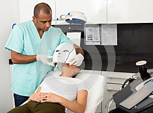 Beautician preparing female client for face phototherapy