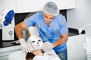 Beautician preparing female client for procedure of phototherapy