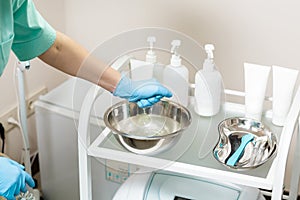 Beautician preparing for procedure. nurse wets sponge in water in bowl. tools in medical basin on table.