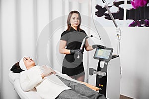 Beautician with radiofrequency device standing by woman in clinic.