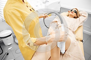 Beautician removes hair with medical laser from legs of beautiful woman in beauty salon, white background