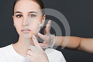 Beautician removes the mask from the face of a young beautiful girl, on a gray background, the concept of rejuvenation