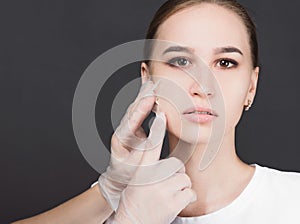 Beautician removes the mask from the face of a young beautiful girl, on a gray background, the concept of rejuvenation