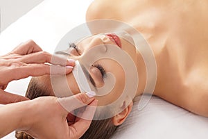 Beautician is removing hair from beautiful female face with hot wax. Woman has a beauty treament procedure. Depilation