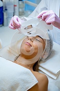 Beautician removing sheet mask on female face for rehydrate face skin, anti aging cosmetic procedure.