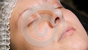The beautician`s hands make markings of a new shape of eyebrows on the patient`s face with the help of special tools, a